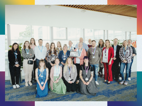 A large group of Open SU staff posing for a photo smiling together, framed with colourful corners.