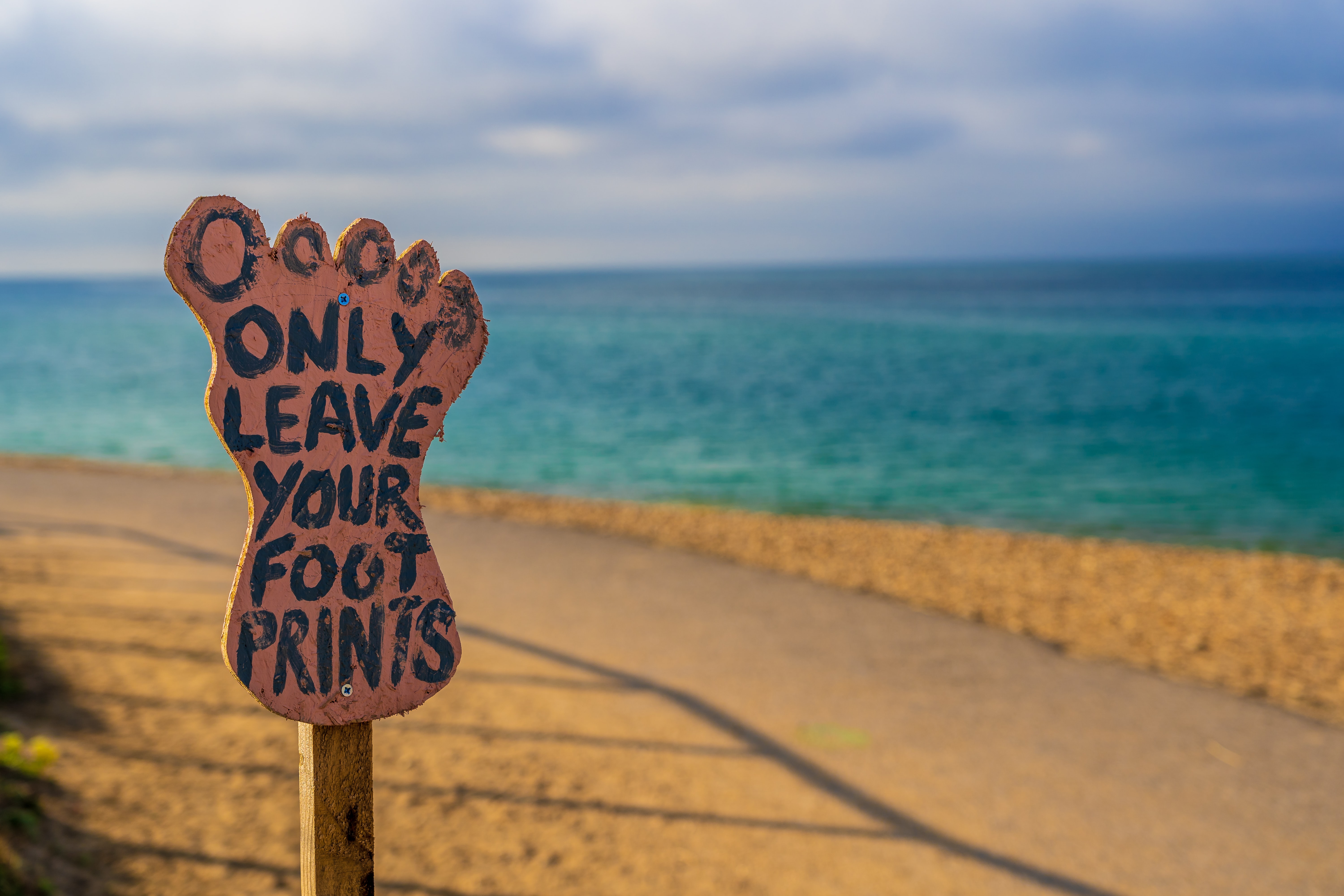A photograph of a beach, with a sign the shape of a human footprint with text that reads 'only leave your footprints'.