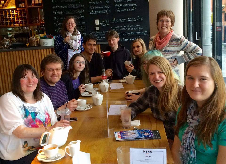 A photo of OU students sat and standing around a table smiling.