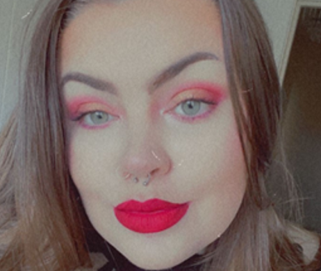 A photo of Hannah smiling, wearing red and pinkish makeup colours.