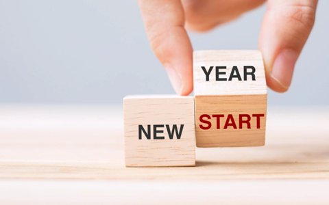 Two cubes, one which reads “New” and the second which reads “Year” on one side and “Start” on the underside, being lifted by a hand