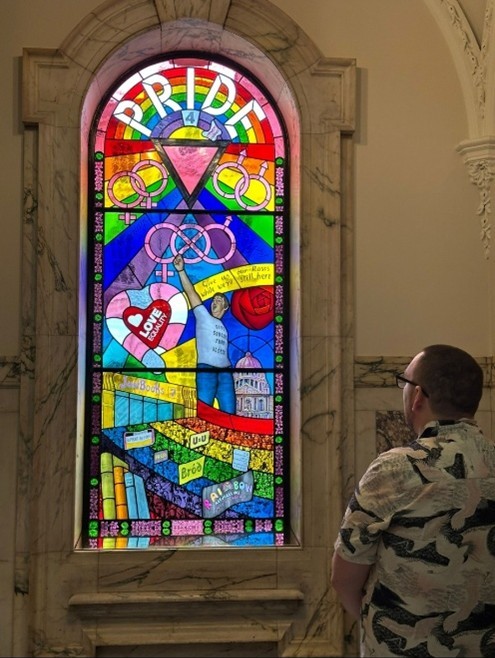 Kevin looking at a stained-glass window, celebrating Pride.