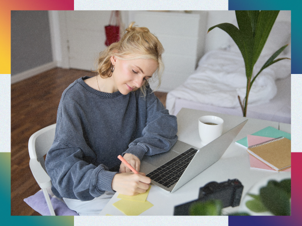 A person sat at a desk writing, framed with colourful corners.
