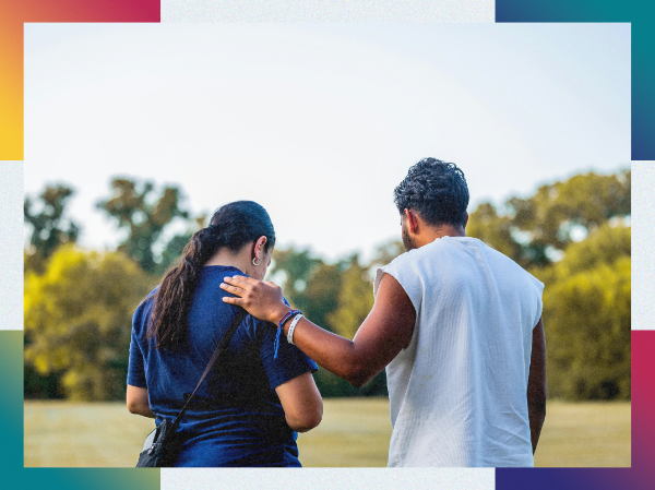 Two people are stood with their backs to the camera. One has got their arm around the other person.
