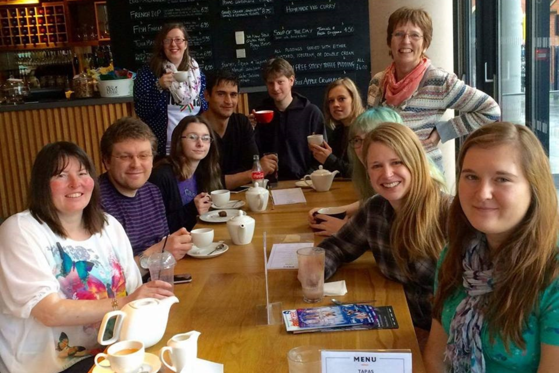 The image shows students sitting in a cafe round a table.