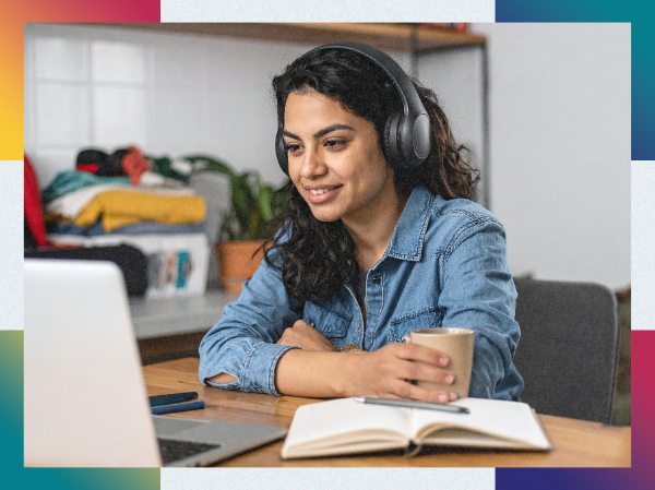 A person wearing headphones and holding a drink looking at their laptop.