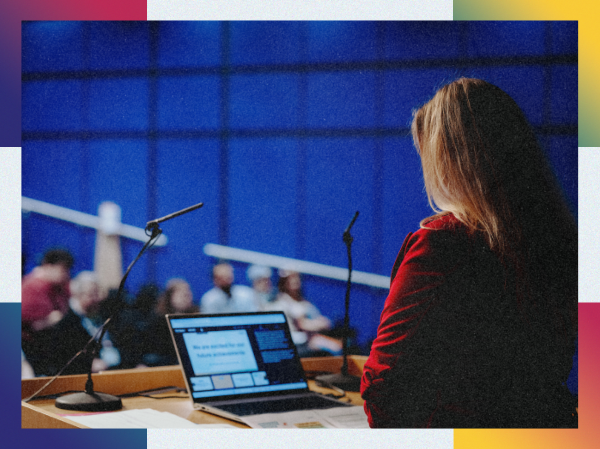A person stood at a podium speaking to an audience with a laptop in front of them, framed with colourful corners.