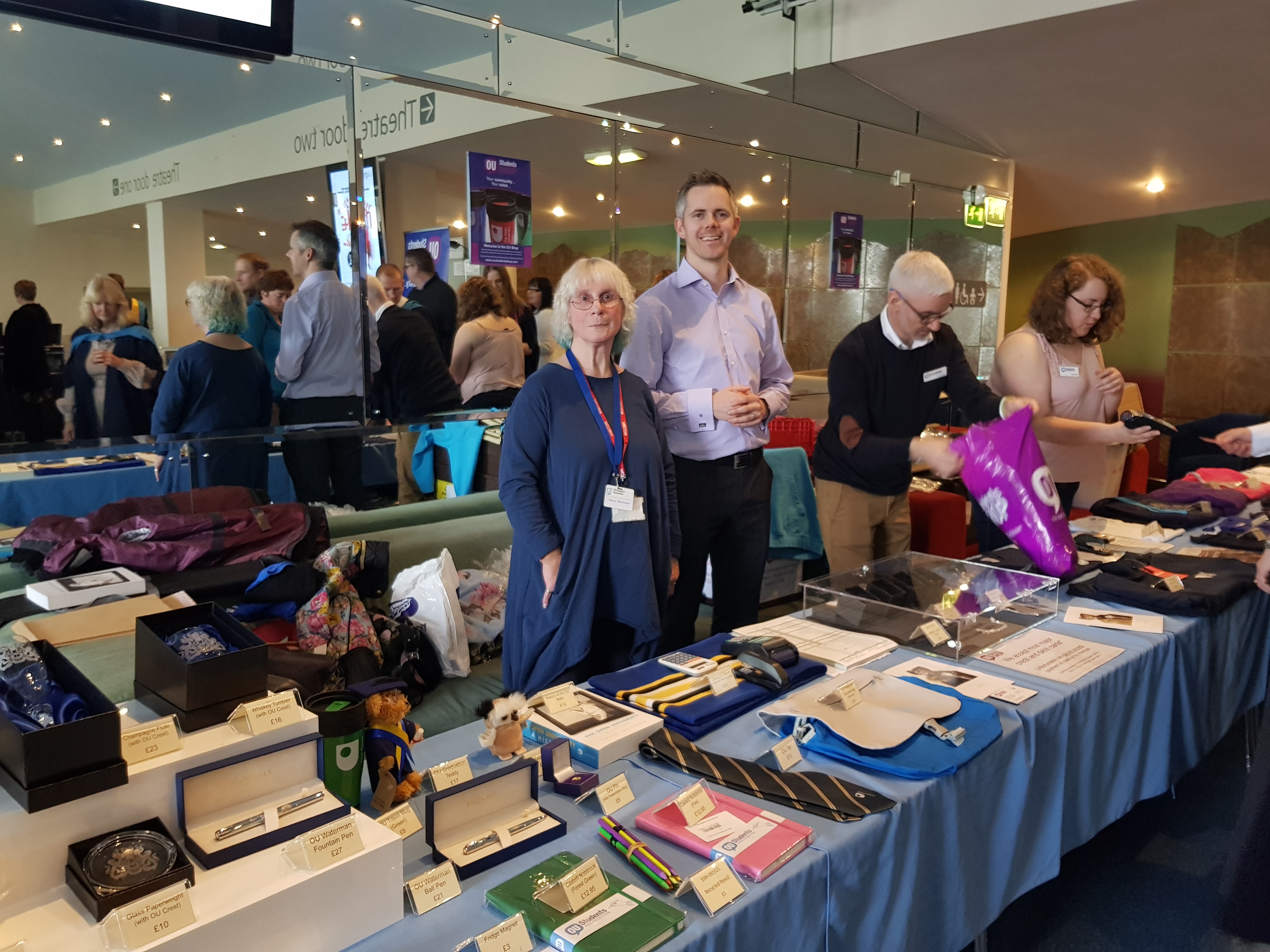 Three graduation volunteers smile at the camera while serving on a graduation stall.